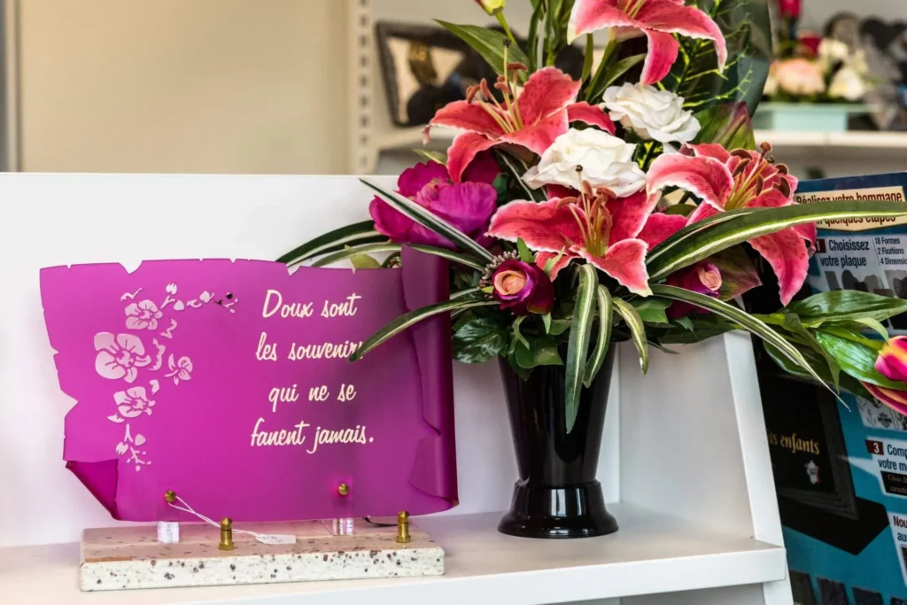 Plaque funéraire personnalisée en forme de parchemin avec fleurs artificielles.